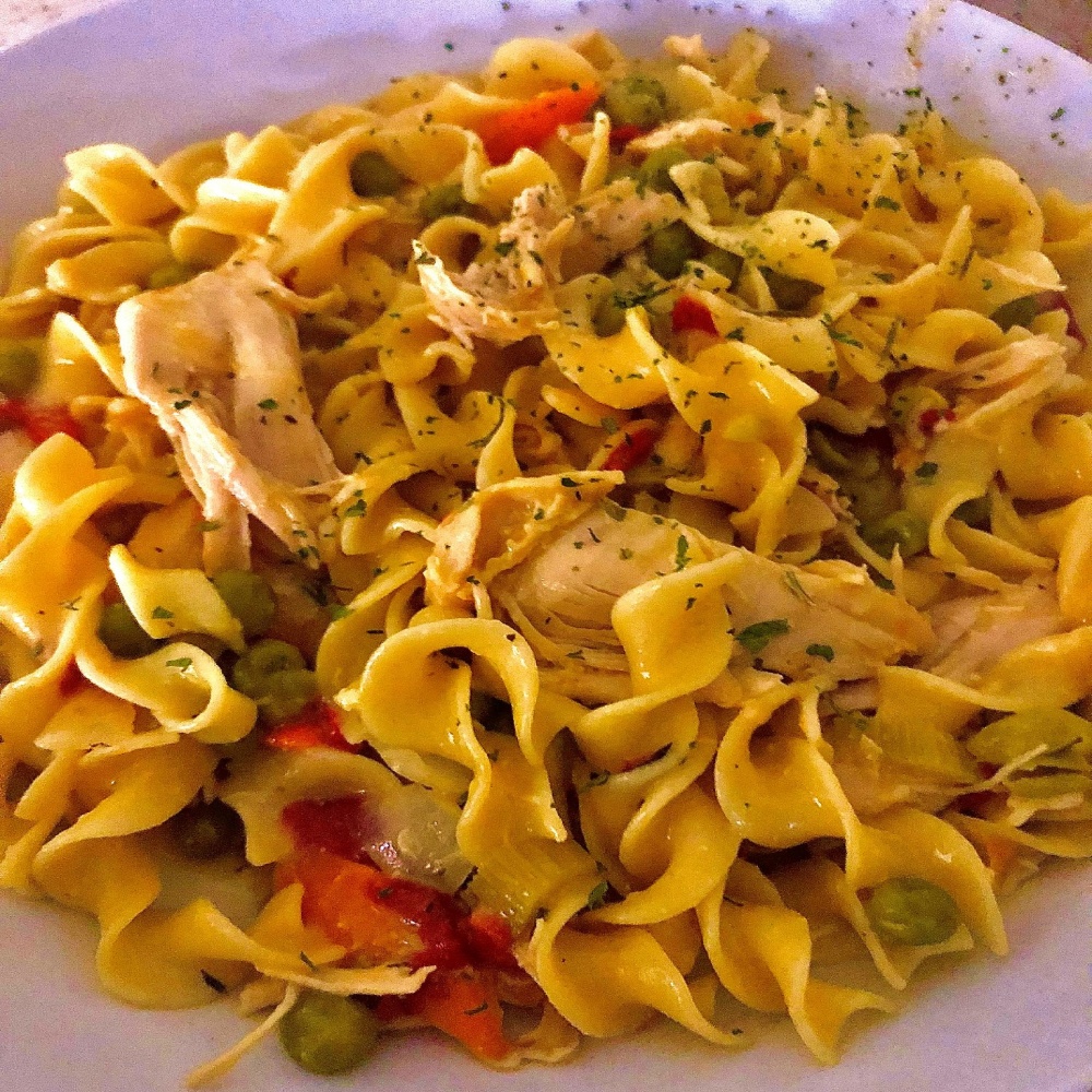 A plate of pasta with chicken, peas and carrots.