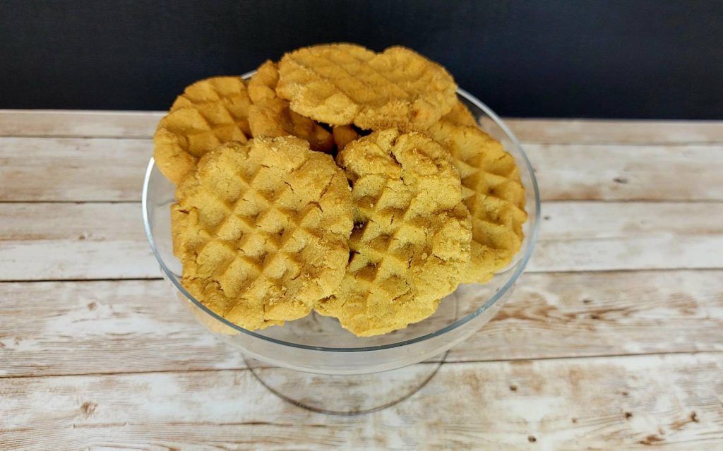 Waffle cookies in a glass bowl on top of a wooden table.