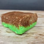 A block of chocolate and green soap on a wooden table.