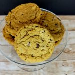 Pumpkin chip cookies in a glass bowl on a wooden table.