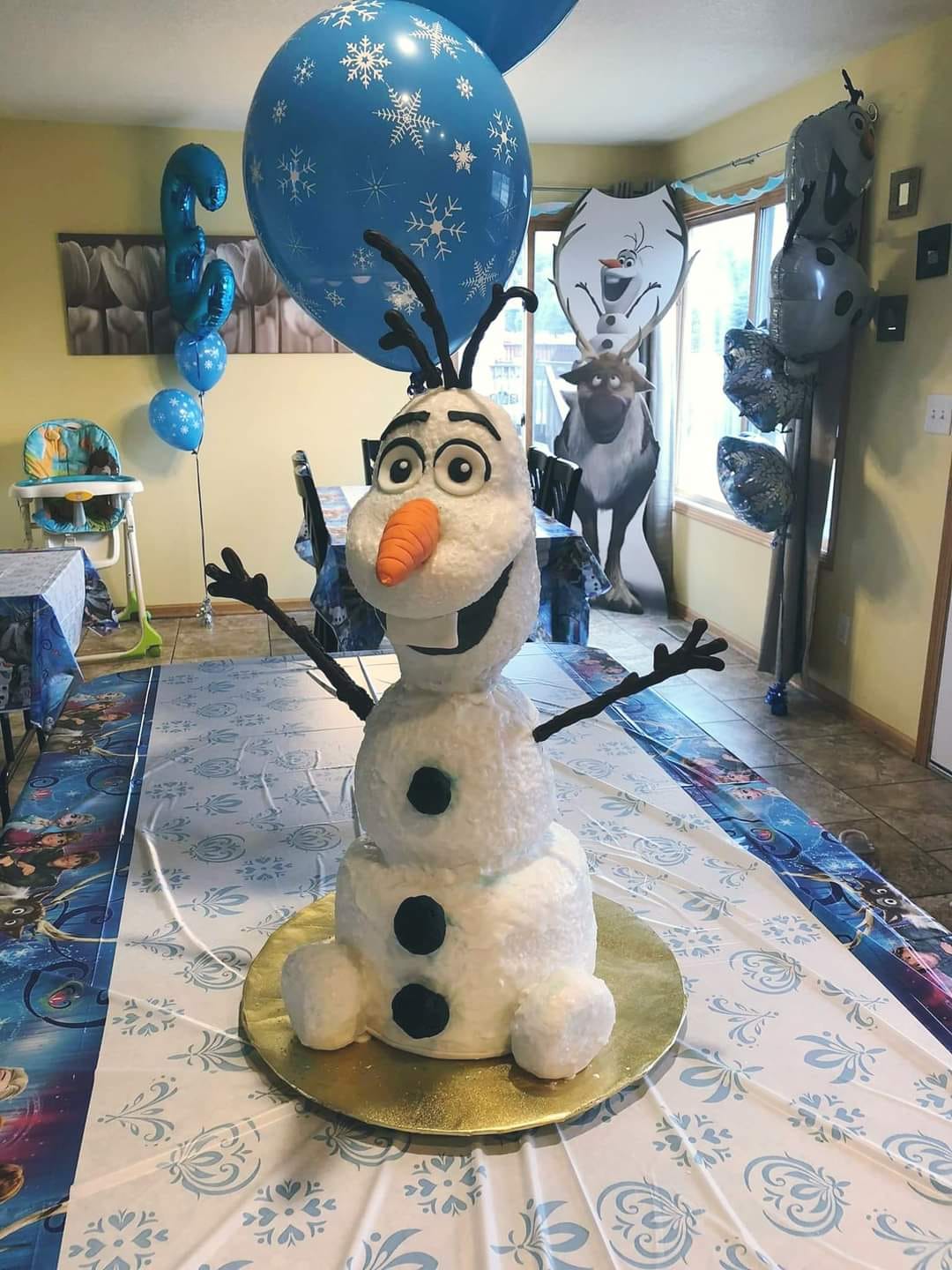Custom frozen olaf cake is sitting on a table in a room.