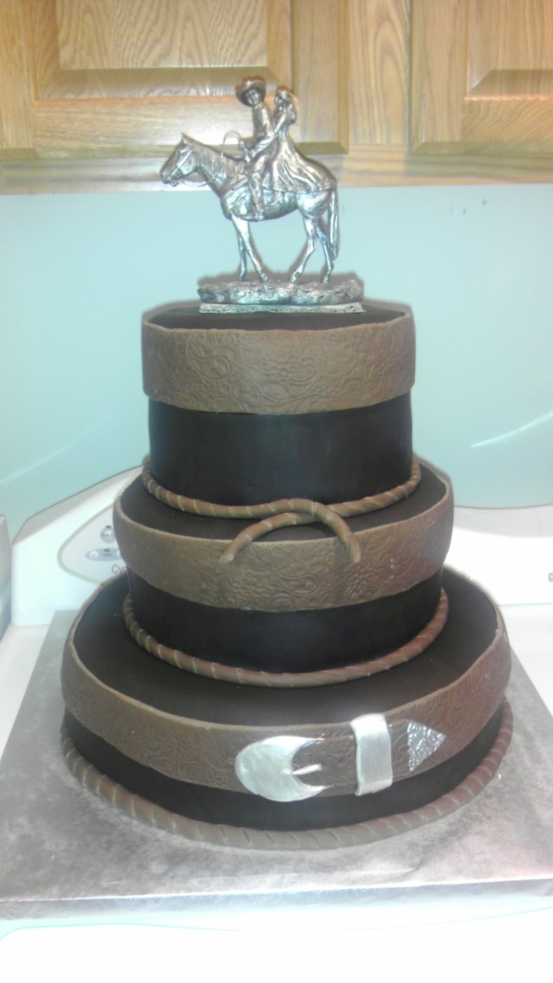 Custom three tier cake with a cowboy figurine on it.Made by Nan's Nummies
