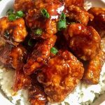 A bowl of asian chicken with rice and green onions.