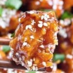 Sesame chicken with sesame seeds on chopsticks.