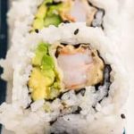 A sushi roll with shrimp and avocado on a blue and white plate.