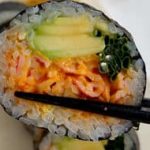 A sushi roll is being held up by chopsticks.