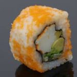 A sushi roll with orange and avocado on a black surface.