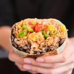 A person holding up a burrito with black beans and rice.