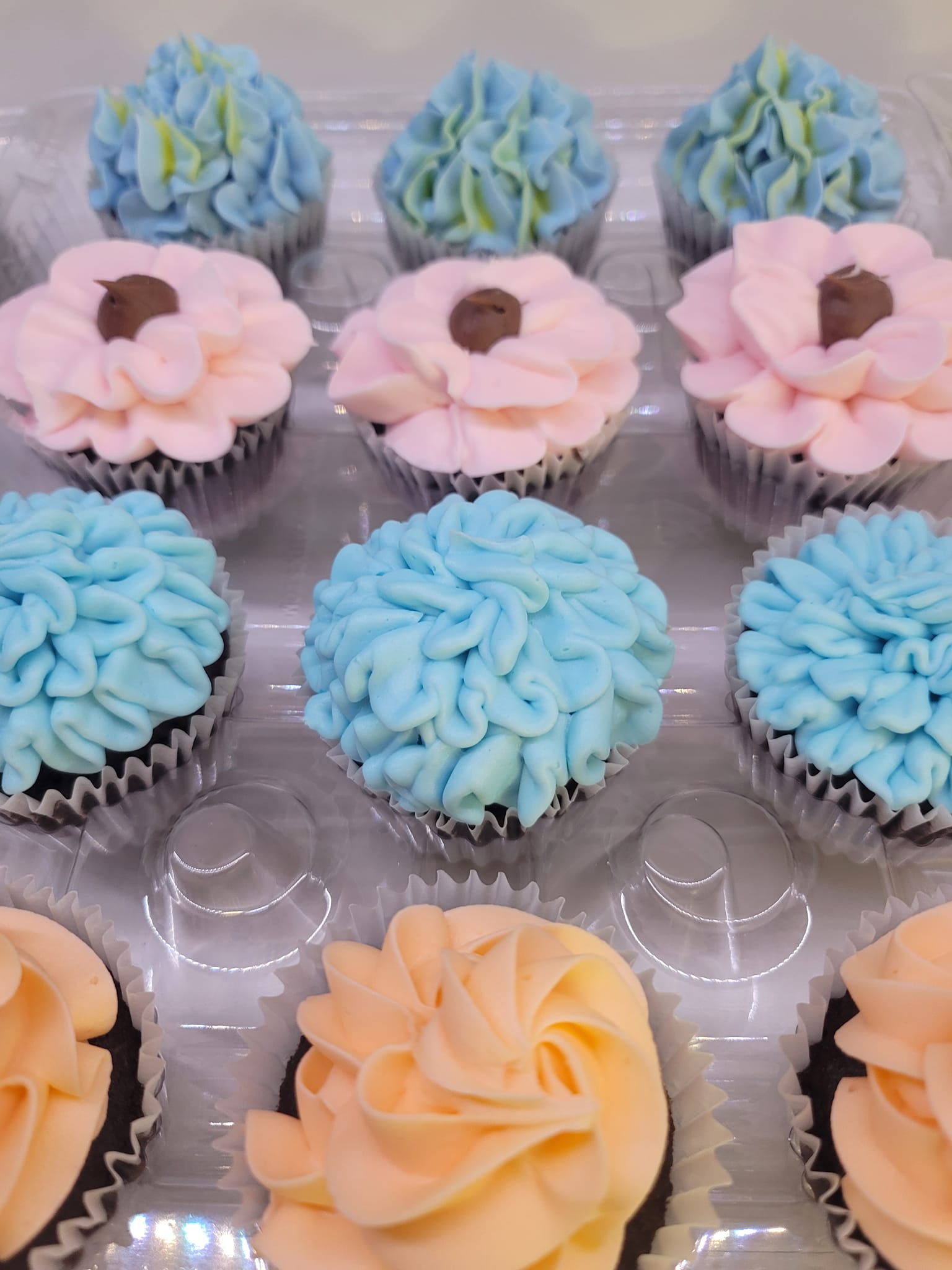 A tray of cupcakes decorated with blue, pink and orange flowers.