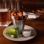 A plate of wings and celery with a glass of beer.