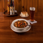 A bowl of stew and a beer on a wooden table.