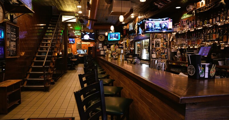 A bar with many stools and televisions.