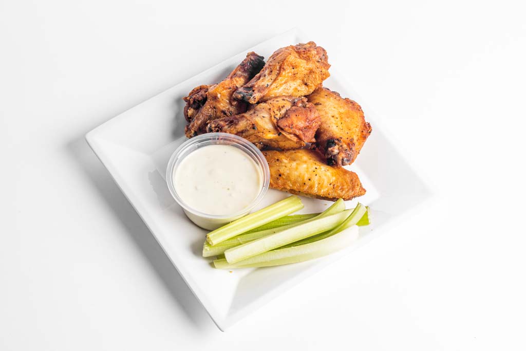 Chicken wings on a white plate with celery and dipping sauce.