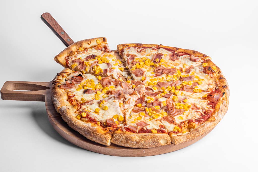 A pizza on a wooden board with a wooden spoon.