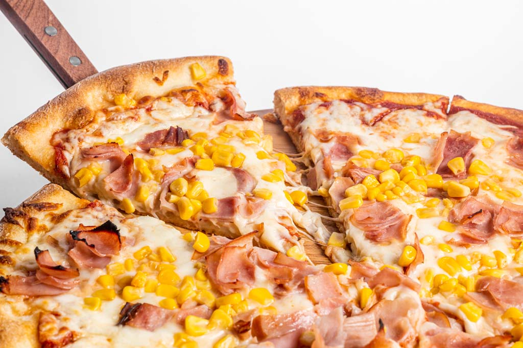 A pizza with ham and corn on a wooden board.