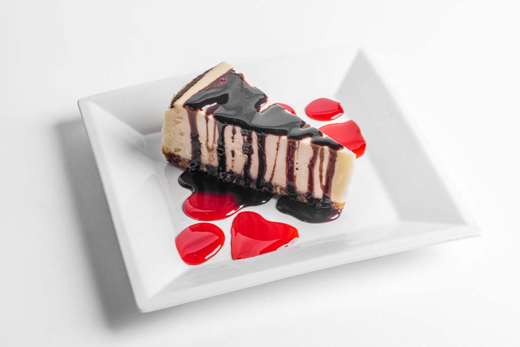 A piece of cheesecake on a square plate with red hearts on it.