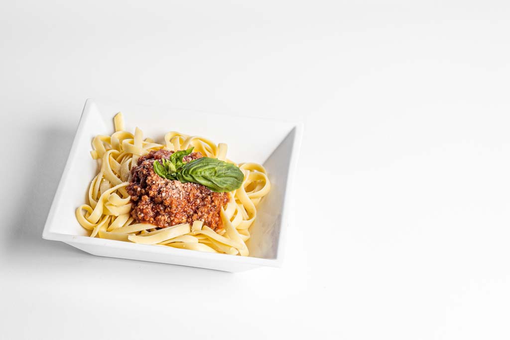 A bowl of pasta with meat sauce on a white background.