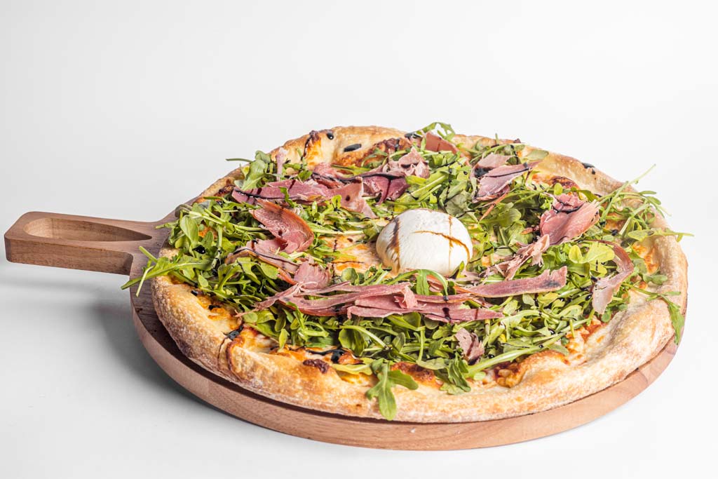A pizza with meat and greens on top of a wooden board.