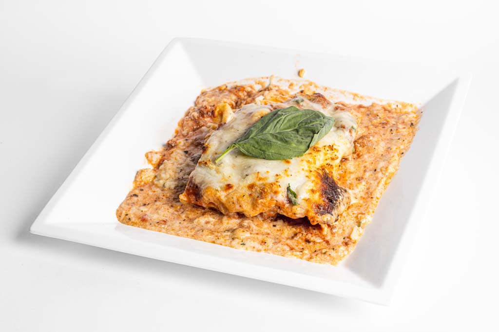 A square plate with a lasagna on it.