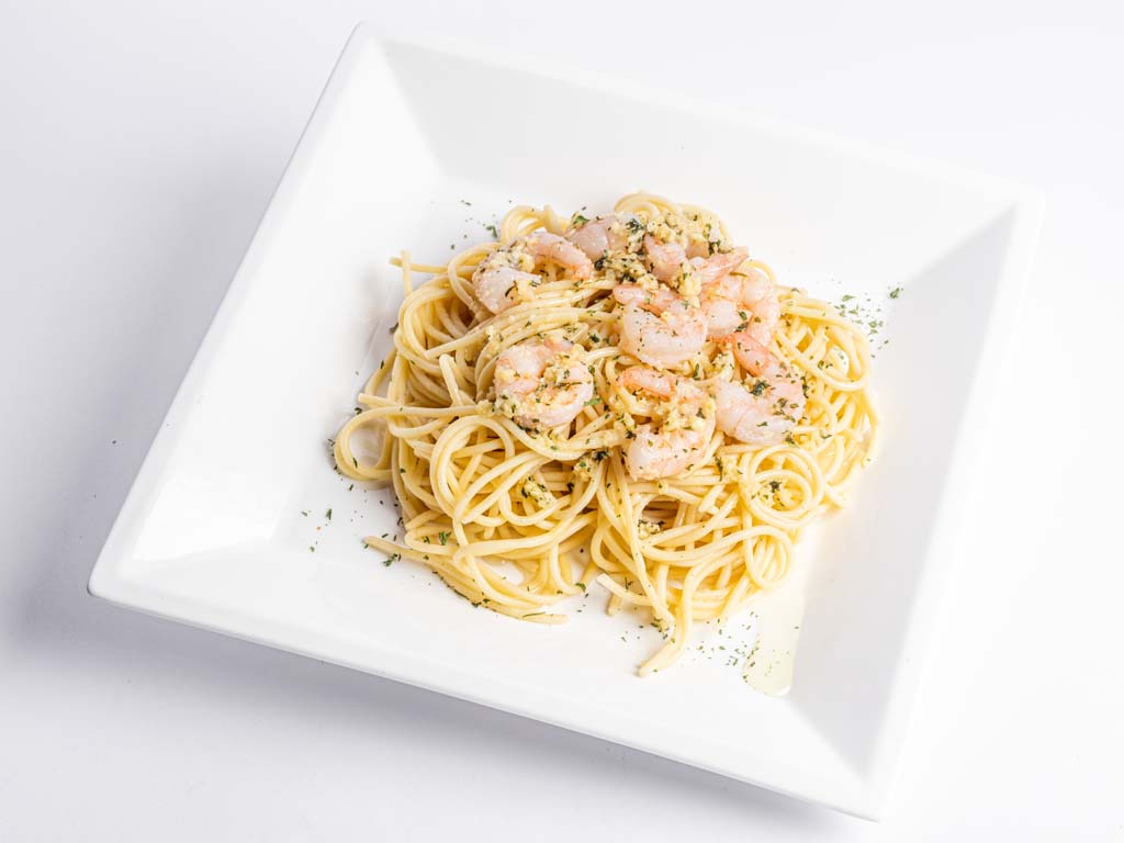 A plate of spaghetti and shrimp on a white surface.