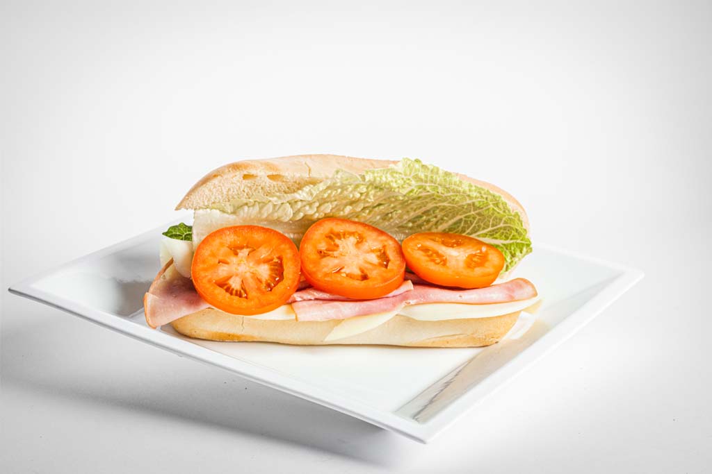 A sandwich with tomatoes, lettuce, and ham on a white plate.