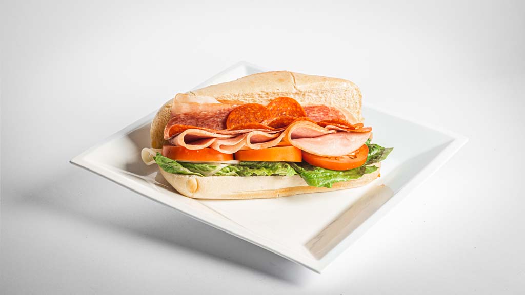 A sandwich with ham and tomatoes on a white plate.