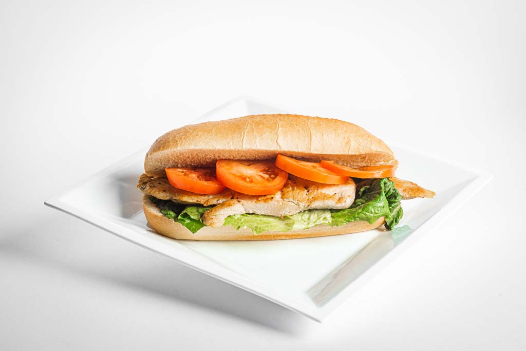 A sandwich with chicken, tomatoes and lettuce on a white plate.