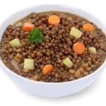 A bowl of lentils and carrots on a white background.