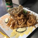 A plate of food with onion rings and a beer on it.