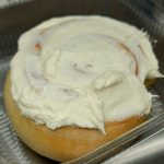 A roll with white frosting in a clear container.