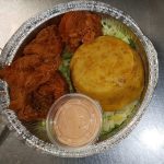 A Takeout Container With Fried Chicken, Cornbread, And A Side Of Sauce On A Bed Of Lettuce.