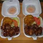 Two Takeout Containers With Fried Chicken, Tostones (fried Plantains), Lettuce, Tomato, And A Side Of Sauce.