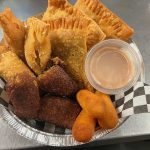 An Assortment Of Fried Appetizers Served In A Foil Tray With Dipping Sauce.