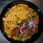 A plate of rice with stewed meat, garnished with red onion and herbs, served on a bed of yellow mashed plantains.