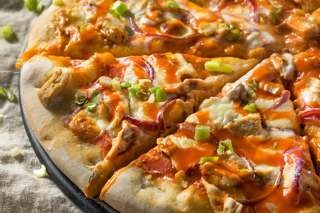 A freshly baked pizza topped with chicken, onions, and a drizzle of buffalo sauce, garnished with chopped green onions.