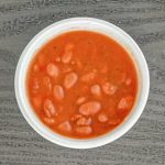 A white bowl filled with red bean soup placed on a gray wooden surface.