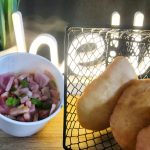 A container of diced vegetables and meat next to a basket holding three pieces of fried bread, with a potted plant and an illuminated "hello" sign in the background.