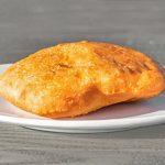 A golden-brown fried bread sits on a white plate against a grey wooden surface background.
