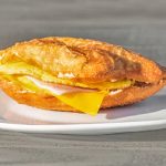 A fried sandwich with egg, cheese, and ham on a white plate.