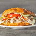 A sandwich with sliced turkey, lettuce, tomato, and cheese served on a white plate.