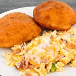 A plate with two fried bread pieces and scrambled eggs mixed with cheese and bacon bits on a gray wooden table.
