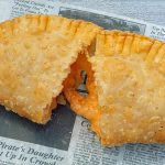 A fried empanada broken in half on a piece of newspaper, revealing its orange filling.