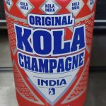 Close-up of a red and white can labeled "Original Kola Champagne India" with small "Kola India" logos around the top.
