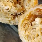 Close-up of a sliced cabbage roll filled with shredded cabbage and a creamy mixture, wrapped in a golden-brown pastry. The dish is displayed on a clear plate.