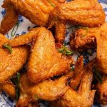 Plate of golden-brown fried chicken wings garnished with small green herbs.