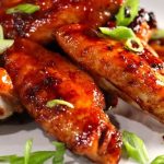 Close-up of glazed chicken wings garnished with sliced green onions on a plate.