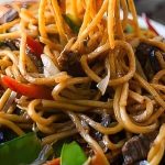 A close-up of stir-fried noodles with beef, bell peppers, snow peas, and onions.