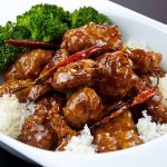 A plate of spicy stir-fried chicken with red chilies, served on white rice, accompanied by steamed broccoli.