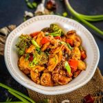 A bowl of stir-fried chicken with broccoli, red bell peppers, and green onions, seasoned in a savory sauce.