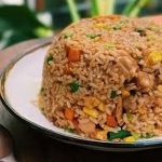 A plate of mixed fried rice with vegetables, chicken, and soy sauce.